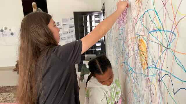 Two participants drawing across a large wall in coloured crayon