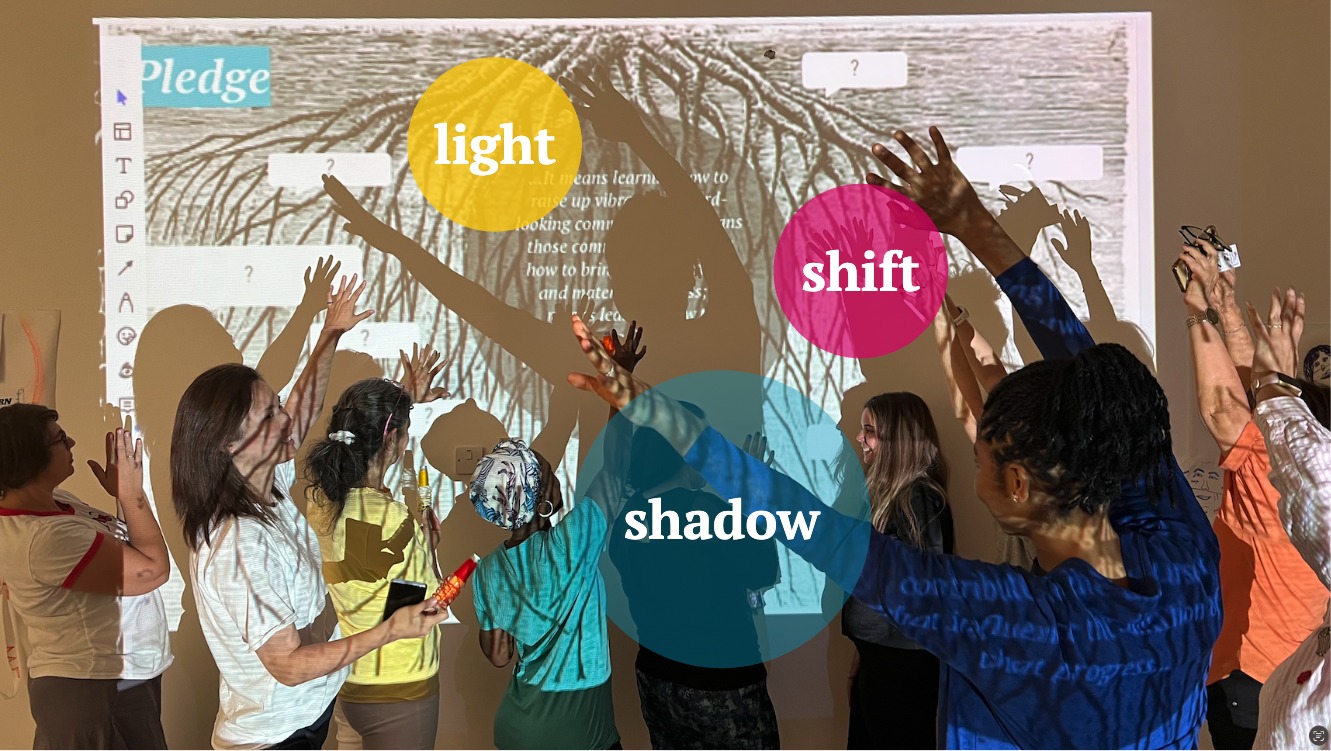 Women reaching up to a projected wall showing overlapping circles of light, shadow, and shift